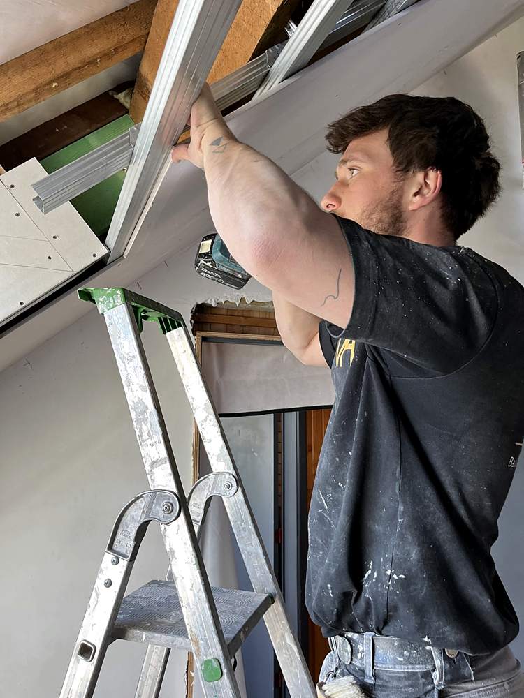 Vakman van HEGI Projects plaatst een profiel onder het dakraam op een zolderwerf